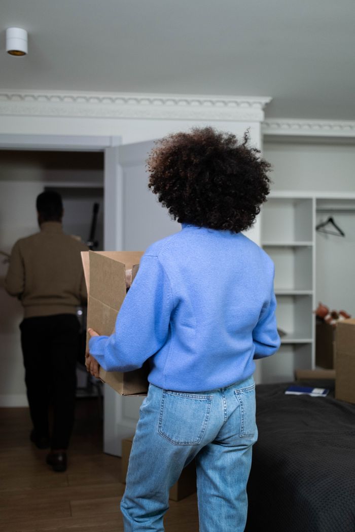 Back view of a woman holding a box at home on moving day, highlighting the theme of relocation and moving.