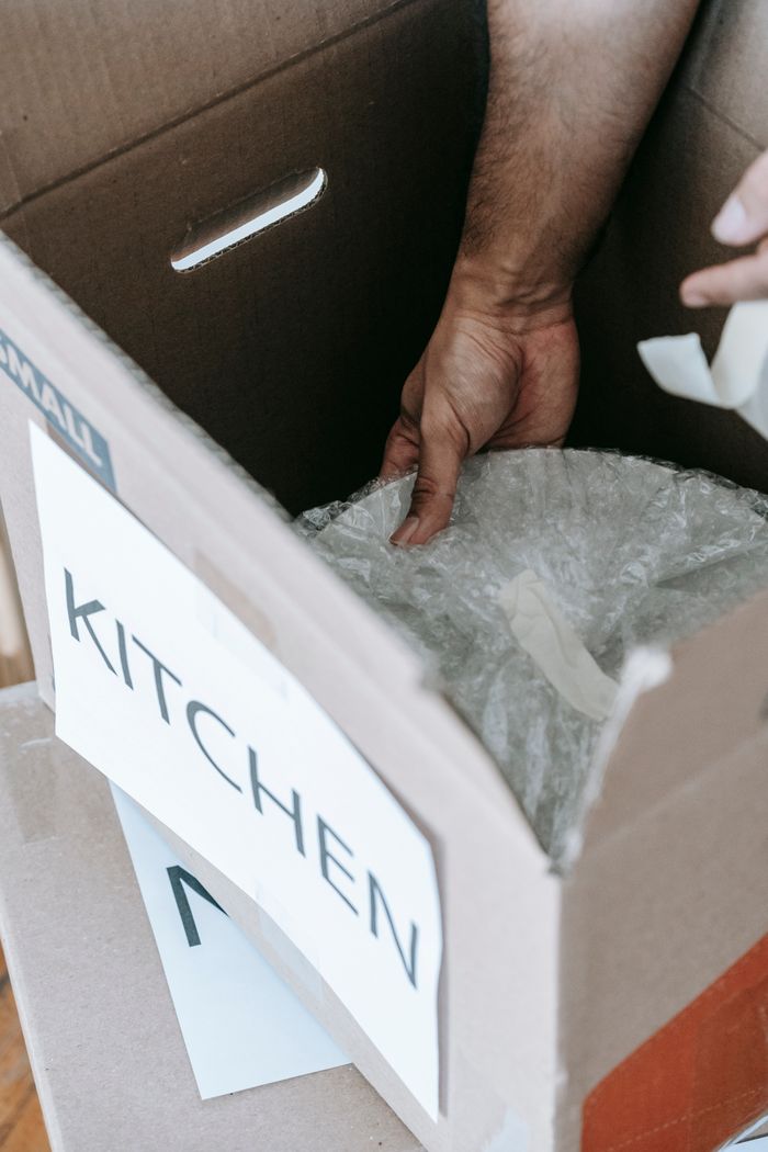 A close-up view of wrapping kitchen items for moving in a labeled cardboard box indoors.